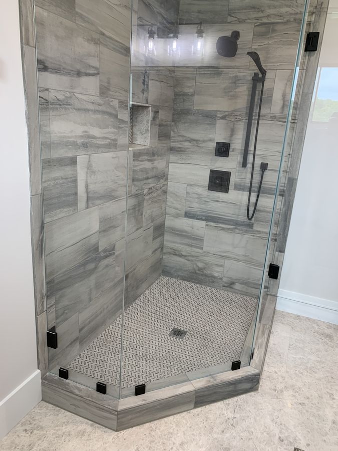Neo-angle shower with grey stone look tile and chevron pan