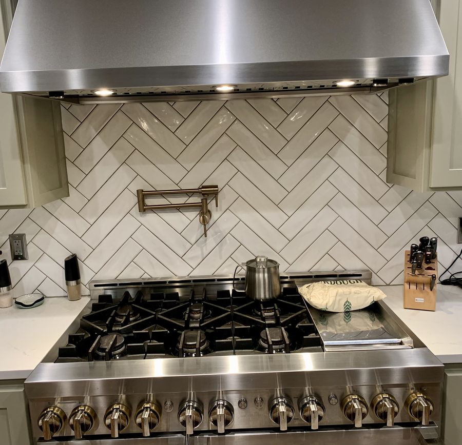 White herringbone marble backsplash behind a professional range and hood